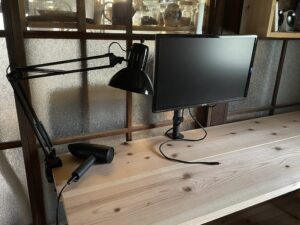 ワークスペースの机。ディスプレイと電気スタンドとドライヤー